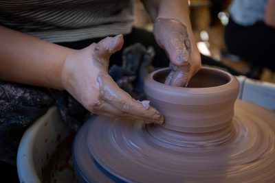 A close-up image of two hands and brown clay on a pottery wheel.