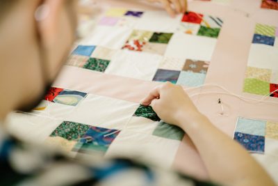 Detail shot of a quilt being crafted by someone who is blurred in the foreground.